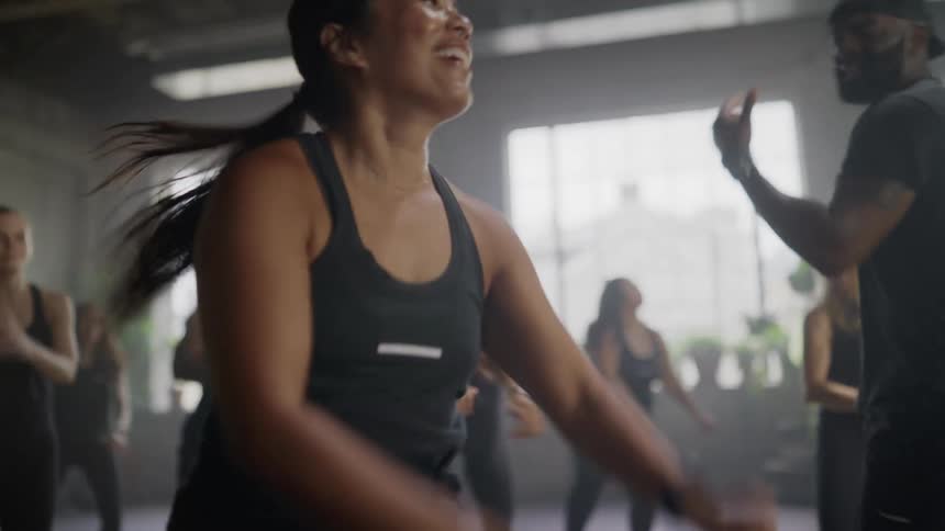 A woman smiles and laughs while energetically participating in a slow-motion group dance fitness class