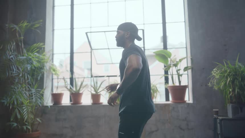 Slow motion of a fit, athletic man dancing in a spacious, sunlit industrial loft studio filled with plants