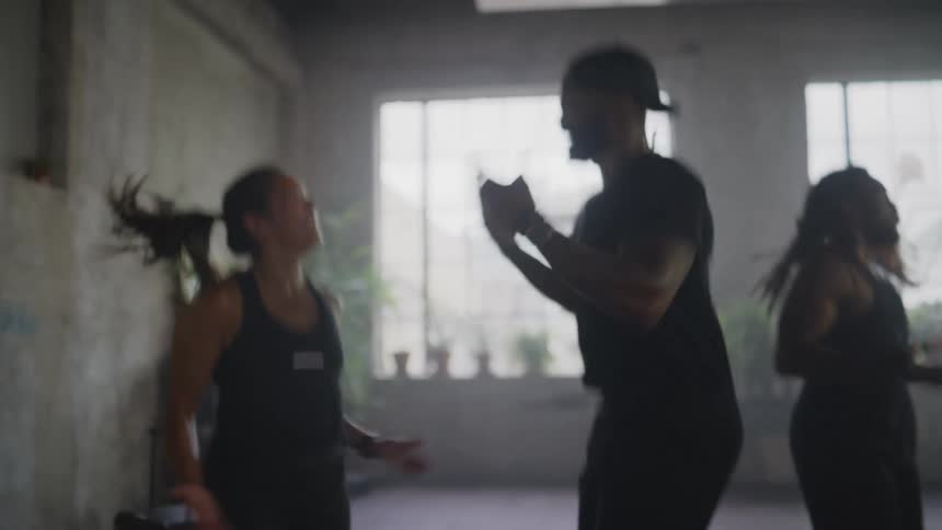 A diverse group of smiling athletes energetically jump and exercise during a high-intensity fitness class in a hazy gym