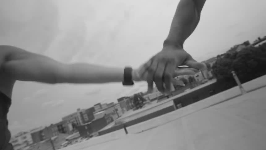 Dramatic black and white slow-motion close-up of a couple reaching for and holding hands on a city rooftop