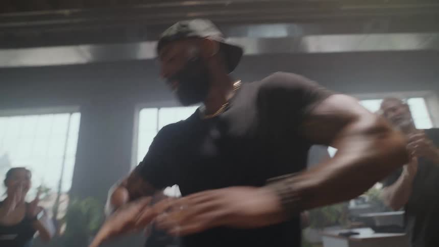 A male dance instructor grooves in a sunlit studio while his enthusiastic class claps along