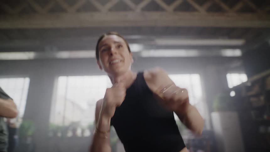 Close-up of a determined and happy woman throwing powerful punches during a shadowboxing fitness class in a hazy gym