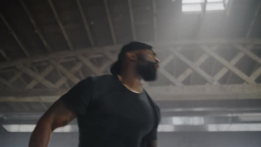 A passionate male instructor with a beard and tattoos energetically leads a dance fitness class in a hazy, backlit warehouse