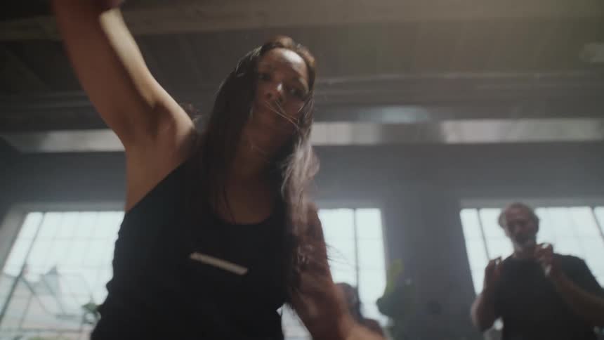 A dynamic woman dances with passion in slow motion during a high-energy group fitness class in a hazy studio