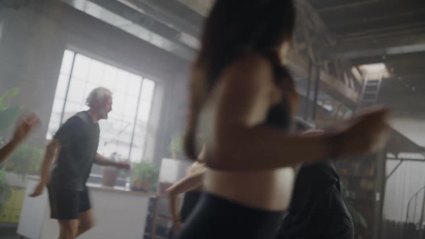 A diverse group of men and women dance together energetically during a high-energy fitness class in a hazy, sunlit studio