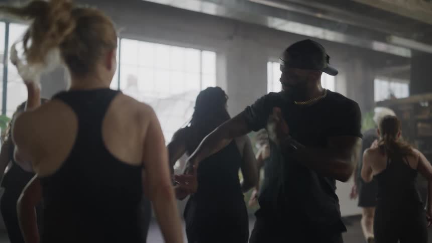 A diverse group of people dance joyfully in a high-energy fitness class led by an enthusiastic instructor in a large studio