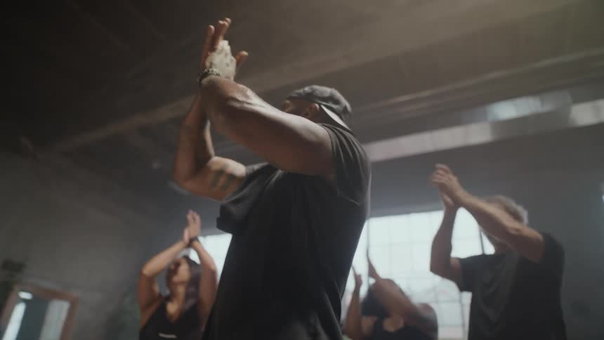 A diverse group of people led by a fitness instructor clap and celebrate in slow motion after a workout in a hazy gym