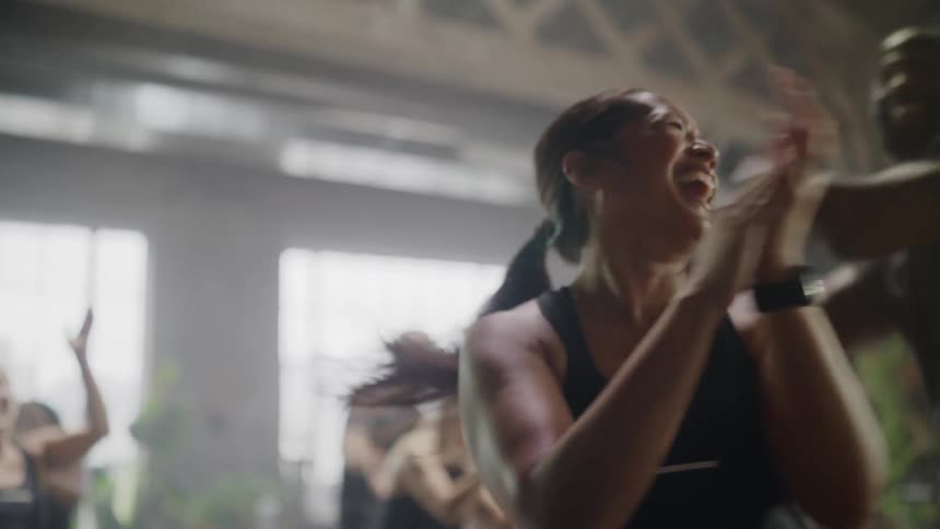 An energetic woman and her trainer laugh and celebrate with their fitness class after a successful workout