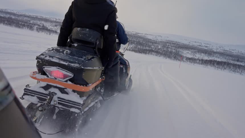 POV shot following a snowmobile driving through a vast, snowy arctic landscape in slow motion