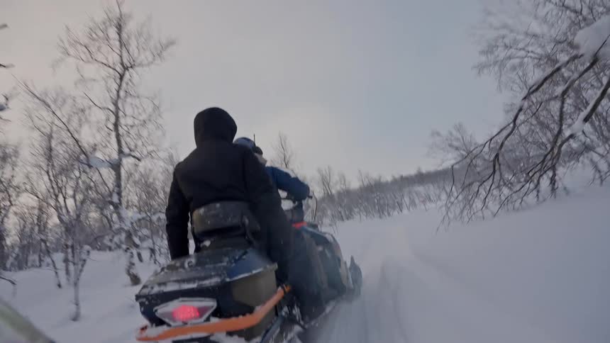 A following shot from behind a person riding on a snowmobile through a snowy forest path in slow motion