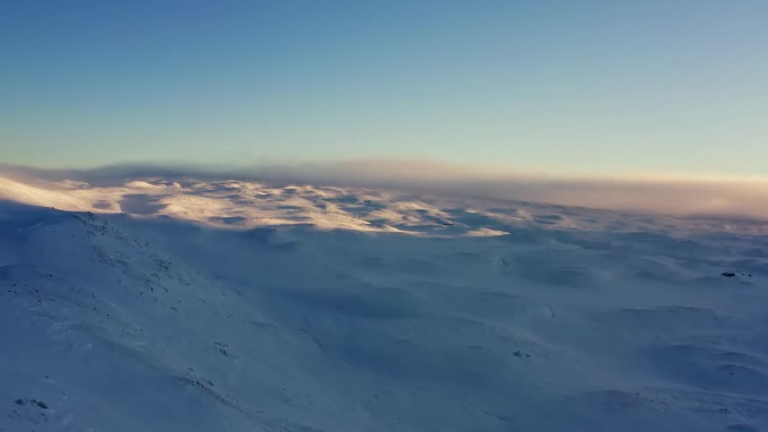 A stunning aerial view captures the serene beauty of a vast, snow-covered mountain tundra at sunrise