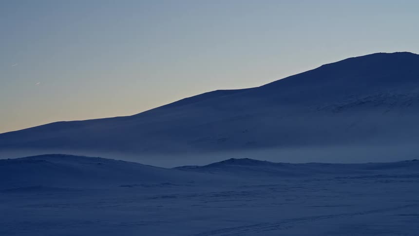 A vast and quiet snow-covered mountain landscape during the blue hour at twilight