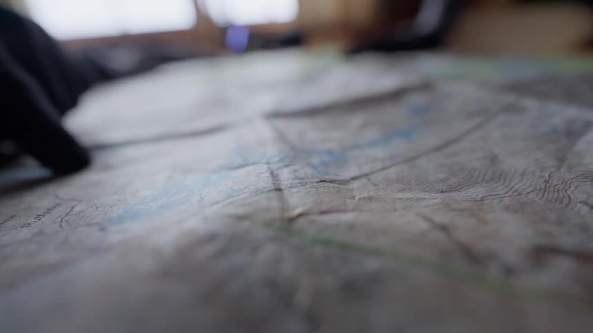 A close-up shot of a gloved finger tracing a path on a well-used topographical map