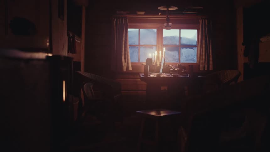 Flickering candles illuminate a quiet, rustic log cabin room with a frosted window, creating a cozy and warm atmosphere