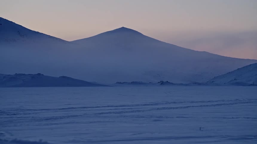 A slow tilt-up reveals a vast, serene, and snow-covered mountain landscape at twilight