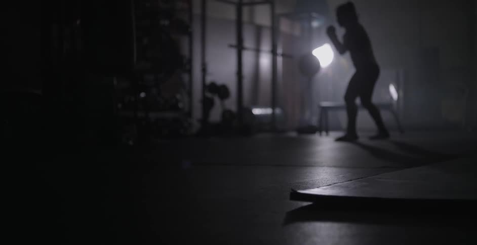 A woman is shadow boxing in a dark gym