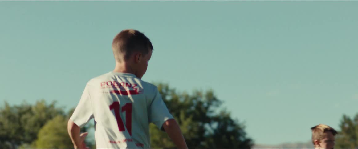 Slow motion shot follows a young boy wearing number 11 as he runs across a green soccer field during a game