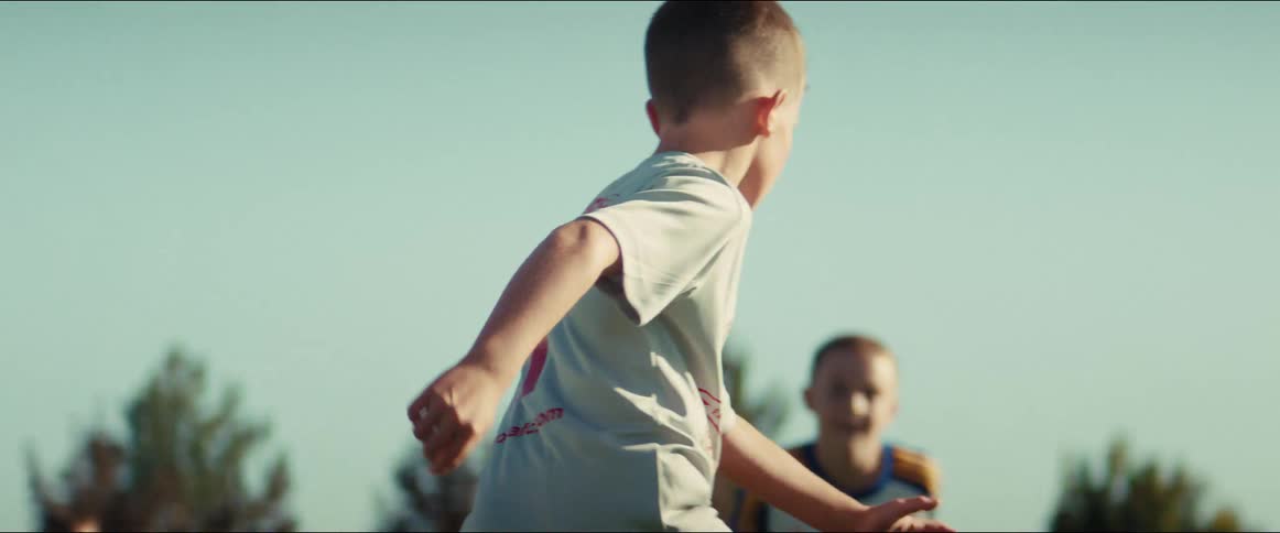 Slow motion footage shows young boys running and competing for the ball during a youth soccer match on a sunny day