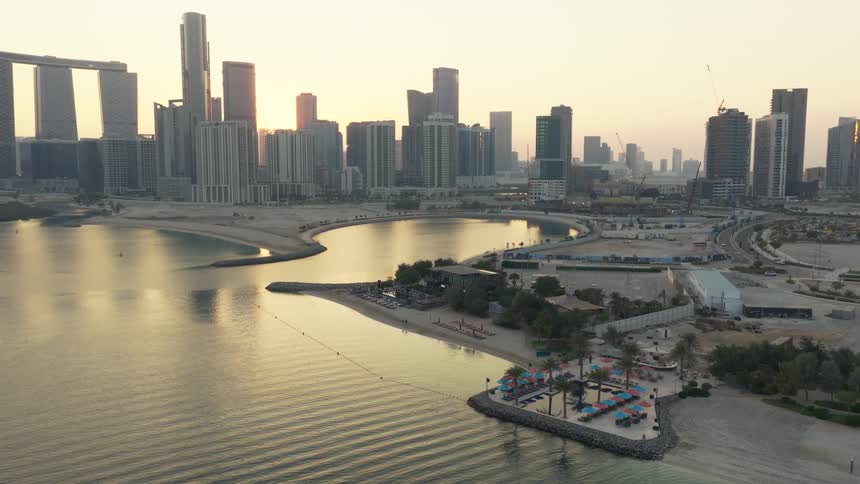 Aerial view of the modern skyline of Al Reem Island in Abu Dhabi, showcasing tranquil beaches and calm waters at sunrise