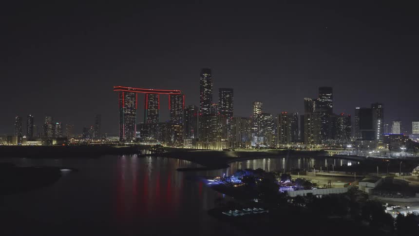 A stunning aerial view of the illuminated Reem Island skyline in Abu Dhabi at night, with city lights reflecting on the calm water