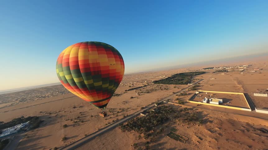 A colorful hot air balloon flies over the vast desert landscape at sunrise