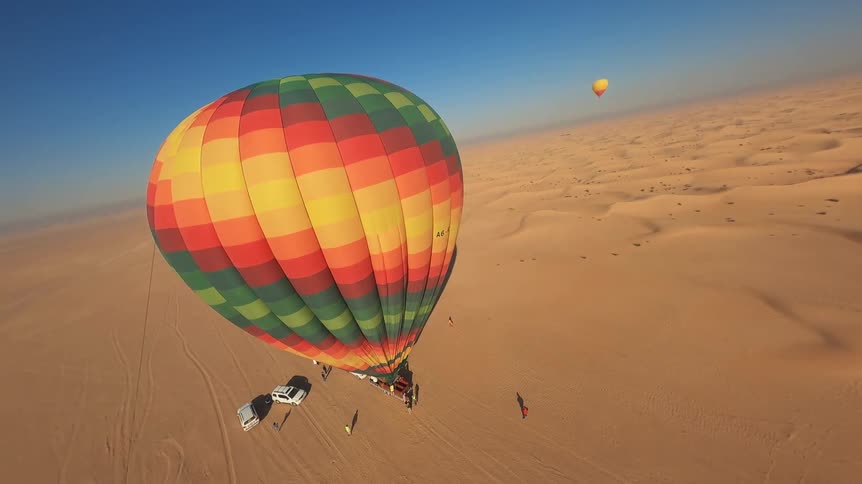 An aerial view from a colorful hot air balloon as it descends for a landing in the vast, sandy desert