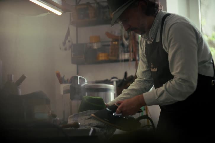 A skilled milliner in his workshop meticulously steams and irons a traditional felt hat