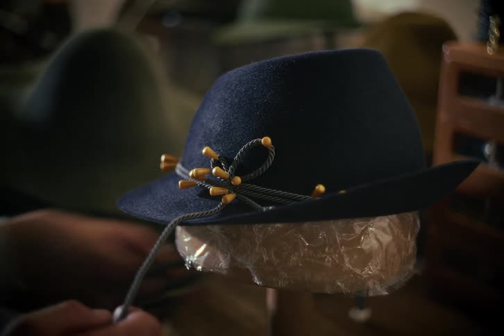 A skilled artisan puts the finishing touches on a handmade, traditional blue fedora hat in a classic workshop