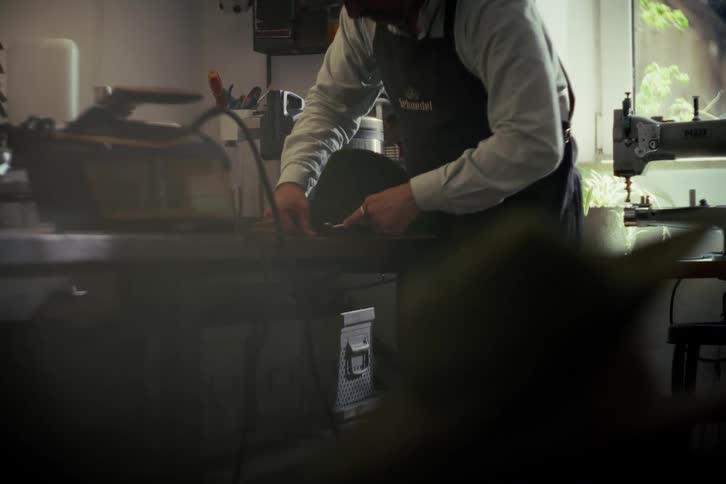 A skilled hatter wearing an apron meticulously steams and shapes a traditional felt hat in his atmospheric workshop