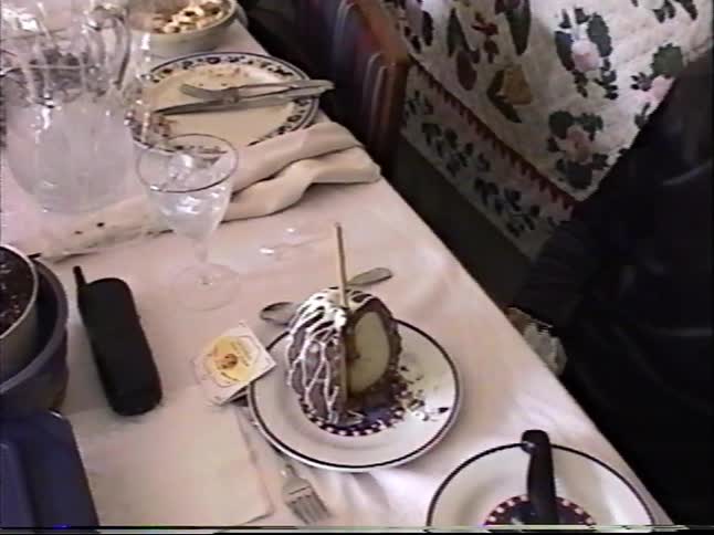 A woman at a dinner table slices and eats a gourmet chocolate-covered caramel apple