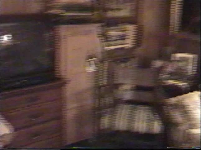 A 90s home video pans from a living room couch to a young boy opening a present, ending on a decorated Christmas tree