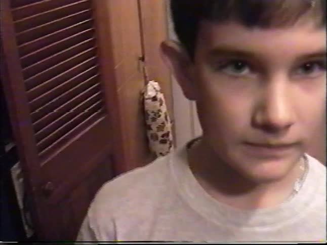 A young boy with a serious expression gets extremely close to the camera in a vintage home video