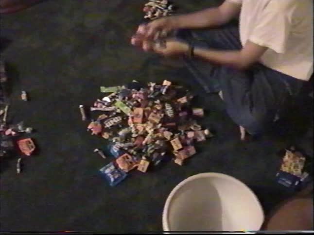 A teenage boy gleefully sorts through a huge pile of Halloween candy on the floor in this home video from the 1990s