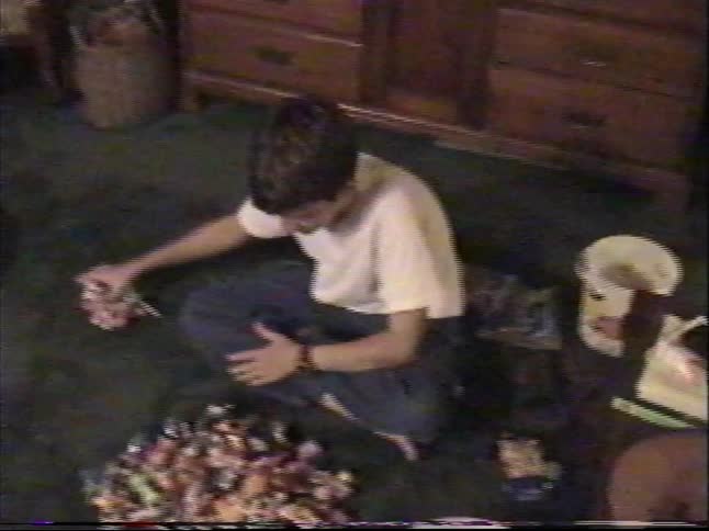 A boy pours out his Halloween candy haul onto the floor and begins to sort through the large pile in this vintage footage