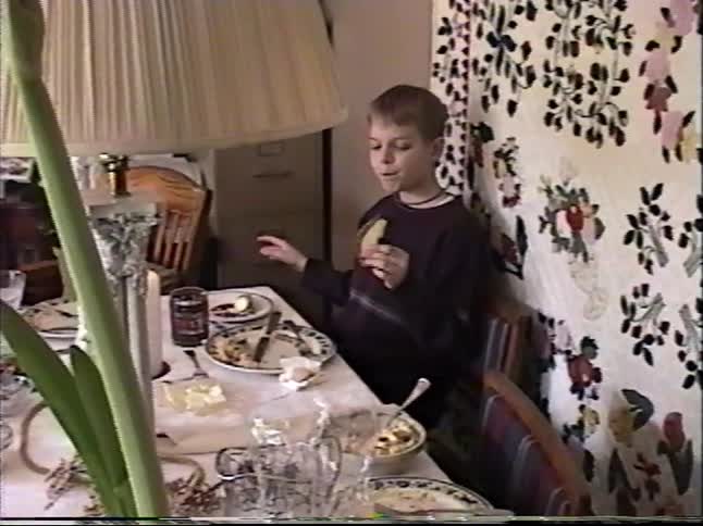 Vintage VHS footage captures two young boys eating and talking at the dinner table during a family gathering