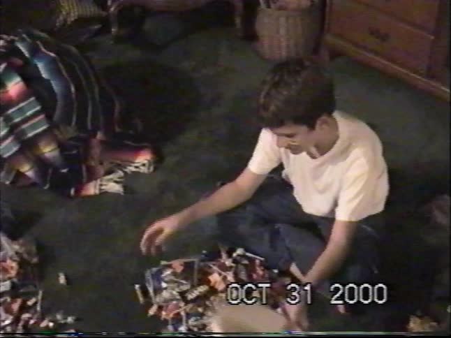 A happy boy with face paint dumps his Halloween trick-or-treating candy onto the living room floor in this nostalgic home video from 2000