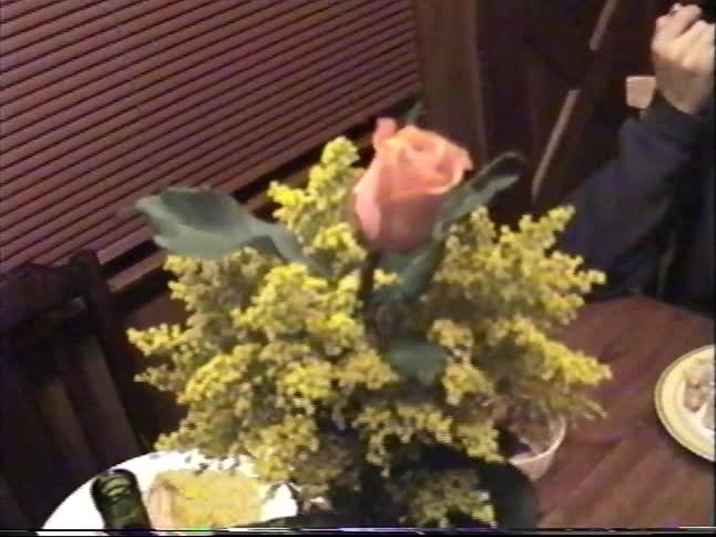 Vintage home video shows a boy eating at a dining table before zooming in on a beautiful rose and yellow flower bouquet