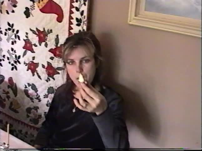 VHS footage of a woman sitting at a dining table eating a piece of a gourmet candy apple during the holidays