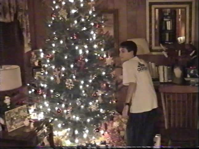 Vintage VHS footage captures a young boy admiring a brightly lit Christmas tree in a cozy, wood-paneled living room