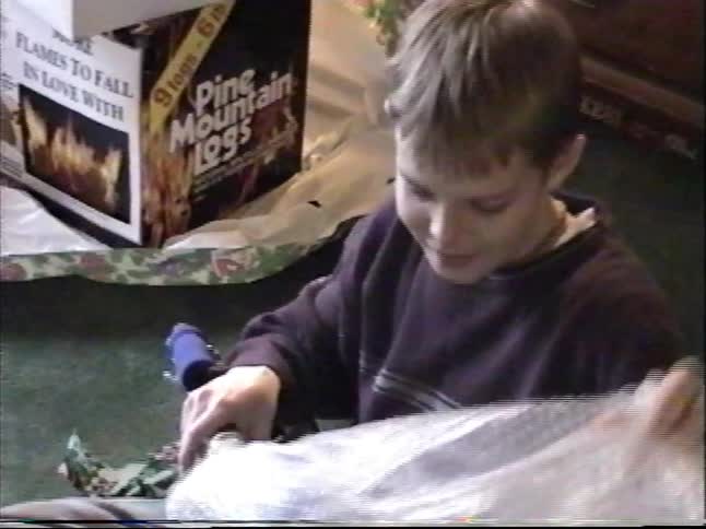 A young boy excitedly unboxes a brand new scooter on Christmas morning in 1999