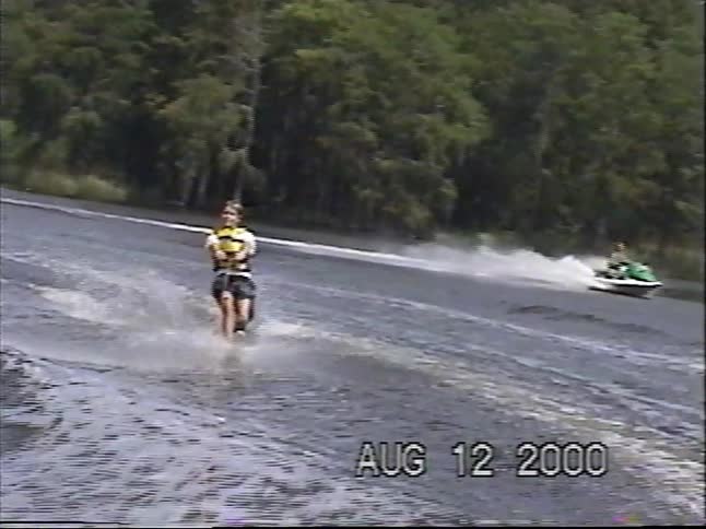 Vintage home movie footage from 2000 captures a person slalom water skiing on a wide river before taking a tumble into the water