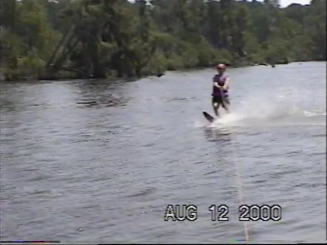 Vintage home movie footage captures a man gracefully slalom water skiing across a calm lake in the summer