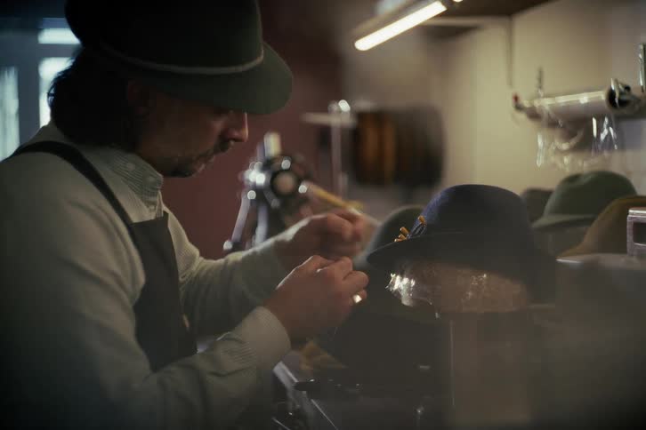 An artisan milliner carefully adds finishing touches to a handmade hat in his studio