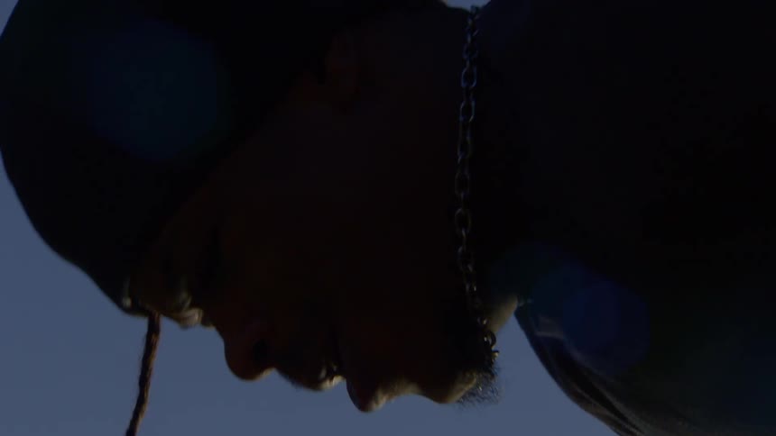 Low angle shot of a person in a hoodie swinging slowly in silhouette against the clear blue sky