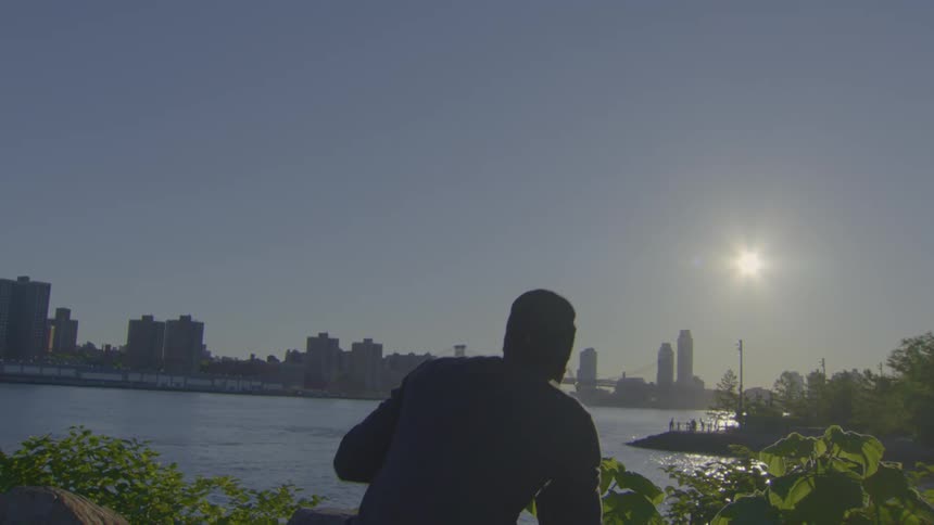 A silhouetted man shadowboxes in slow motion with a city skyline in the background as the sun shines brightly