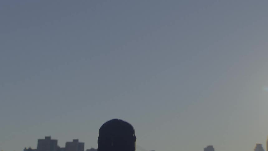 Slow motion shot of a man's silhouette from behind as he dances with a city skyline in the background