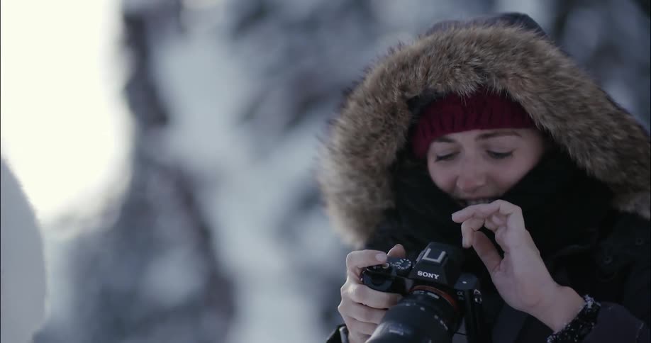 A woman adjusts her camera in the snow