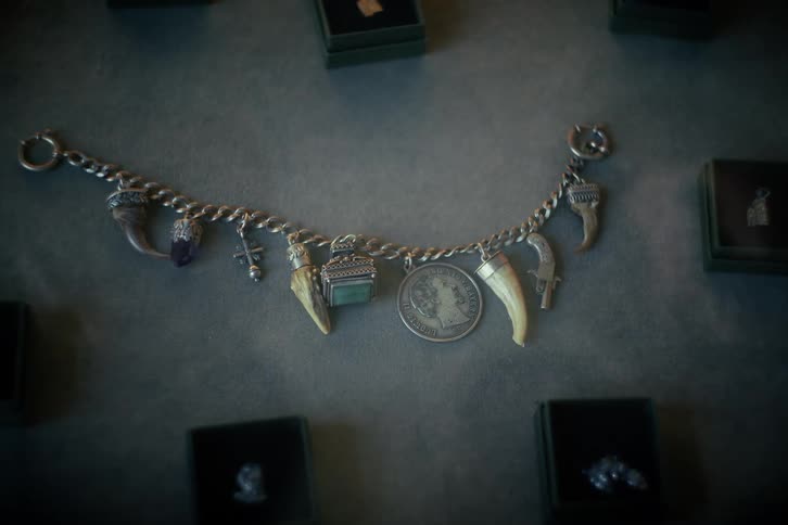 A mysterious antique silver charm bracelet with various talismans and amulets is displayed on a dark surface