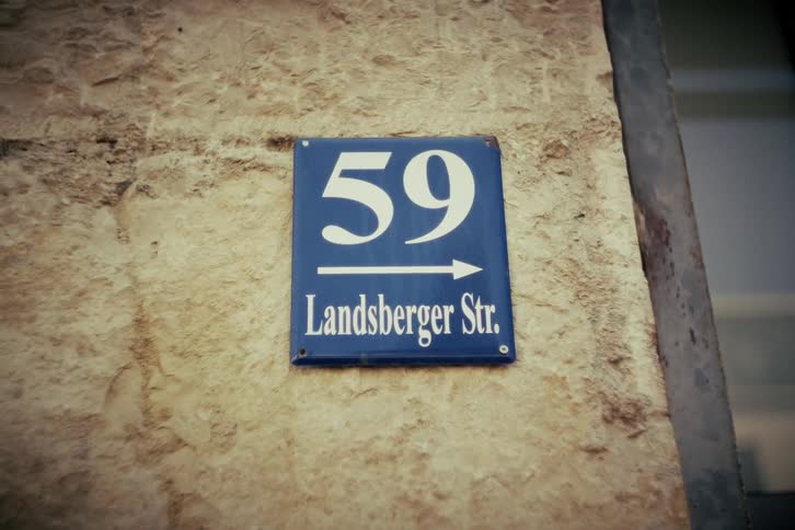 A close-up of a blue and white street sign for Landsberger Strasse 59 mounted on a rustic stone wall