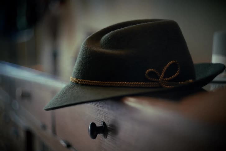 A slow rack focus reveals a classic green felt fedora resting on a vintage wooden cabinet in a dimly lit room